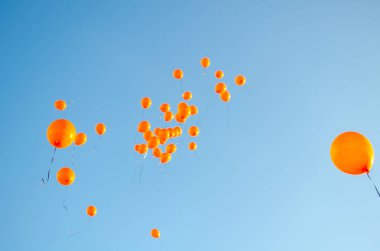 Orange balloons rising to the sky, balloons released against blue sky