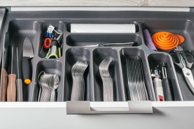 Beyaz mutfak dolabı açık çekmecede gümüş çatal, kaşık, bıçak ve diğer aksesuarlarla siyah çatal bıçak takımı var. Mutfak depolama sistemi