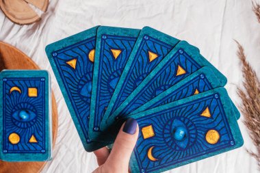 Mavi tırnaklı el, tahta tepsi ve çivili beyaz kumaş çarşafın üzerine yayılmış Tarot kartları tutuyor. Üst Manzara. Minsk, Belarus - 09.27.2021