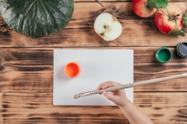 Adım adım Cadılar Bayramı çocukları özel balkabağı elması baskıları. Dördüncü adım: Çocuk eli, boya fırçasını turuncu guaj boyasının yanında tutuyor. Üst görünüm