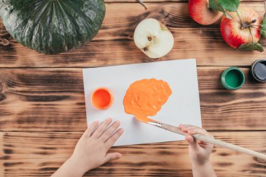 Step-by-step Halloween childrens tutorial pumpkin apple prints. Step 5: Childrs hands brush orange gouache paint onto paper. Top view clipart