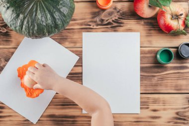 Adım adım Cadılar Bayramı çocukları özel balkabağı elması baskıları. Altıncı adım: Çocuk eli, elmanın yarısını turuncu guaj boyasına batırır. Üst görünüm