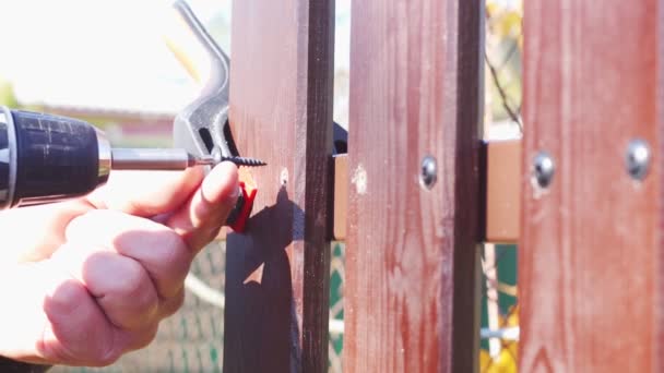 Manlig hand med skruvmejsel driver skruv för att fixa brunt staket ombord på gården. Slow motion närbild video — Stockvideo