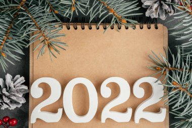 Mutlu yıllar 2022. Beyaz numaralar 2022, katlanmış defter üzerinde Noel ağacı dalları ve çam kozalakları var. Mutlu noeller. Üst Manzara. Boşluğu kopyala