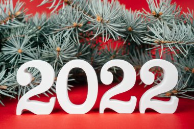 Mutlu yıllar 2022. Beyaz ahşap numaralar 2022 kırmızı arka planda yemyeşil Noel ağacı dalları ile ayakta duruyor. Mutlu Noeller..