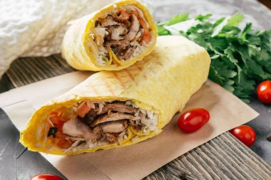 Tavuklu ve sebzeli klasik shawarma dürümü. Pita ekmeği, ahşap arka planda, kiraz domatesli ve yeşil maydanozlu.