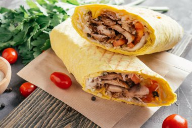 Tavuklu ve sebzeli klasik shawarma dürümü. Pita ekmeği, ahşap arka planda, kiraz domatesli ve yeşil maydanozlu.