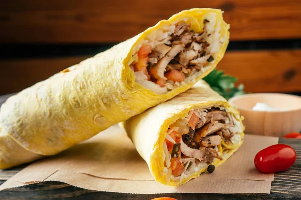 Tavuklu ve sebzeli klasik shawarma dürümü. Pita ekmeği, ahşap arka planda, kiraz domatesli ve yeşil maydanozlu.