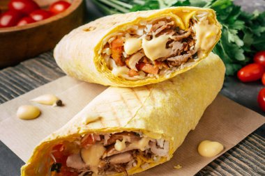 Peynir soslu bir rulo shawarma, Pita ekmeğinde tavuk ve sebze, ahşap arka planda, kiraz domatesli ve yeşil maydanozlu.