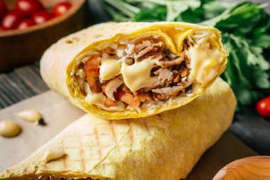 Peynir soslu bir rulo shawarma, Pita ekmeğinde tavuk ve sebze, ahşap arka planda, kiraz domatesli ve yeşil maydanozlu.