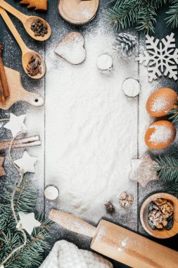 Noel ağacının dalları, zencefilli kurabiyeler, aksesuarlar ve siyah ahşap masaya serpilmiş un parçaları. Uzayı kopyala Mutlu Noeller ve mutlu yıllar. Üst Manzara. Dikey
