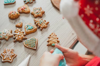 Çocuğun kısmen bulanık elleri mutfakta mavi kremayla zencefilli kurabiye süslüyor. Çocuk ahşap masada kurabiye hazırlar. Mutlu Noeller, mutlu yıllar.
