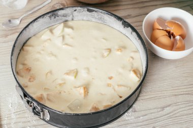 Çiğ elmalı turta hamurlu fırın tabağı mutfak tezgahında duruyor, yumurta kabuklu kâsenin yanında.