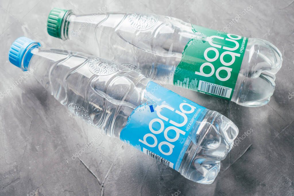 Plastic bottles of Bonaqua mineral water lie on gray concrete surface. Bottles with green and blue labels inscribed with medium sparkling and still water in Russian. Minsk, Belarus - 12.11.2021