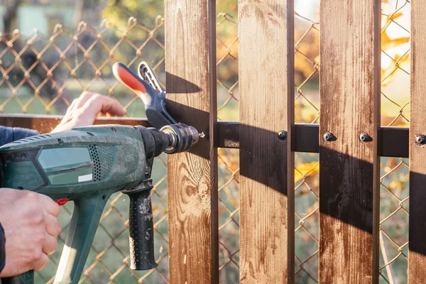 Main de charpentier tenir perceuse électrique pour faire un trou dans la construction de planches en bois à la construction métallique pour reconstruire la clôture. — Photo