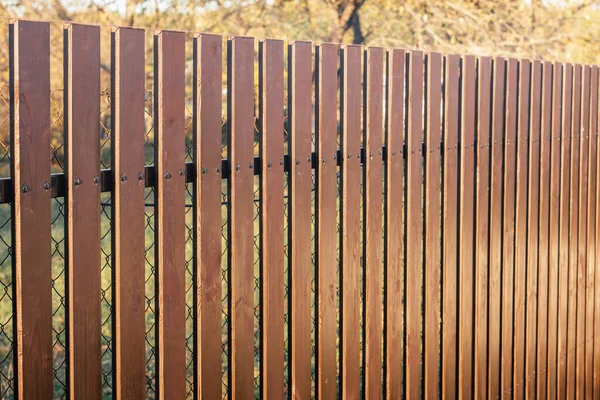 Nueva cerca marrón de madera moderna en el fondo de la cerca de eslabón de cadena alrededor de árboles amarillos de cerca — Foto de Stock