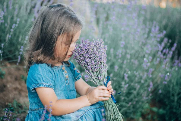 Kot elbiseli siyah saçlı 3-4 yaşlarında küçük bir kız oturmuş leylak demeti kokluyor.
