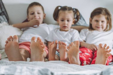 Üç kardeş çıplak ayakla yatakta yatıyor. Çocukların bacaklarına odaklan. İki kız ve bir oğlan, arkadaşlar ya da aile