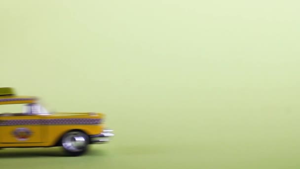 A yellow toy taxi car on a pastel yellow background drives into the frame and stops. Taxi service. — Video