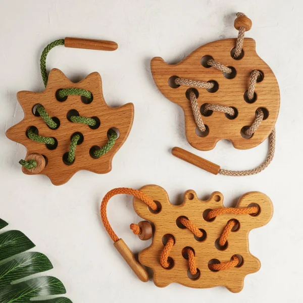 Přírodní dřevěné hračky různých tvarů s otvory pro výuku tkaní se zelenými, béžovými a oranžovými šňůrami s rostlinami. — Stock fotografie