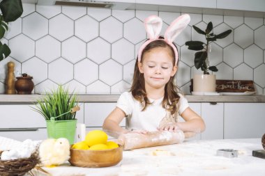 Özenle gülümseyen küçük bir kızın portresi, yemek pişirme, hamur hazırlama, unlu merdane. Paskalya pastası kurabiyeleri yapıyorum.