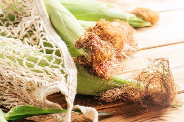 Dört taze taze mısır kremalı mısır koçanı kulağı, ahşap arka planda, yeniden kullanılabilir ekolojik alışveriş poşetinde.