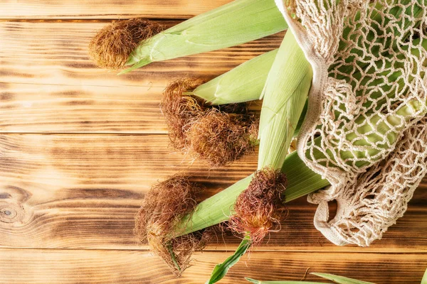 Dört tane taze yeşil mısır kremalı mısır koçanı yaprakları ve ahşap arka planda yeniden kullanılabilir ekolojik alışveriş torbası. Üst Manzara. Boşluğu kopyala