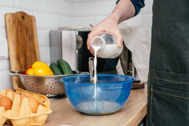 Tanınmayan adamın elleri, şişeden mavi plastik kaseye, çelik kevaşenin yanındaki masaya tel çırpıcıyla süt döker..