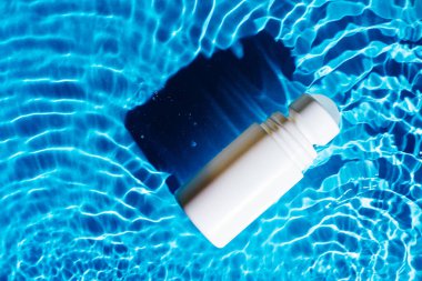 Beyaz güzellik ürünü terleme önleyici deodorant, ter kokusu, şeffaf tatlı su şişesi, benekler ve dalgalar, koyu gölgeler. Sıcak yaz plajında cilt bakımı koruması. Düz yatıyordu.