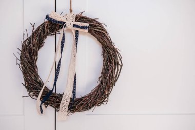 Dekoratif beyaz bant dantelli Wickers 'dan örülmüş kahverengi söğüt ağacı çelengi. Arka plan olarak beyaz duvar. Geleneksel mevsimlik etnik bayram dekorasyonu. Selamlama ve uğurlu sembol. Boşluğu kopyala