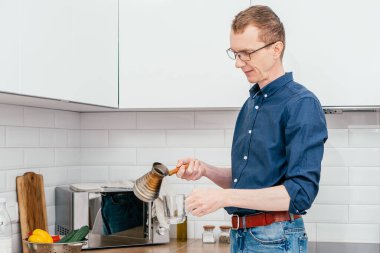 Orta yaşlı, kısa kızıl saçlı, mavi gömlekli bir adam sabah beyaz mutfakta, tahta saplı, taze, sıcak, doğal kahveyi camdan bir kaba döküyor. Evde kahve yapıyorum..