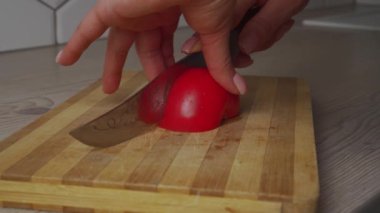 Çıplak manikürlü orta yaşlı kadın elleri mutfak ahşap atölyesinde bambu tahtasında bıçakla kırmızı domates kesiyor. 4k video