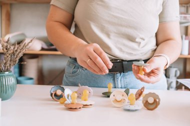Kırpılmış iş kadını elleri, yeni doğmuş bebekler için beyaz masada silikon emzikler yapmak ve tasarlamak. Küçük işletme, mağaza. Çocuklar için yumuşak malzeme seçiyorum. Doğal ekolojik aksesuarlar.