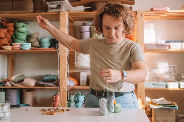 Doğal güvenli aksesuarlar yapan bir kadın. Masanın üzerinde, eko tarzı. Boncukları diziyorum. Ivır zıvır çıngırağı süslemeli bir oyuncak. Bebek dişleri çiğnemek için el yapımı oyuncaklar. Adım adım. Çocuk mağazası