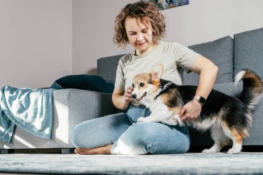 Kıvırcık saçlı, neşeli, çıplak ayaklı, köpek Corgi 'si olan kadın. İtaat eğitimi, evcil hayvan besleme, oturma, dinlenme ve koltuğun yanındaki rahat oturma odasında oynama. Hafta sonu boş zaman aktivitesi
