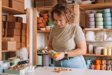 Doğal güvenli aksesuarlar yapan bir kadın. Masanın üzerinde, eko tarzı. Boncukları diziyorum. Ivır zıvır çıngırağı süslemeli bir oyuncak. Bebek dişleri çiğnemek için el yapımı oyuncaklar. Adım adım. Çocuk mağazası