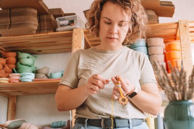 Doğal güvenli aksesuarlar yapan bir kadın. Masanın üzerinde, eko tarzı. Boncukları diziyorum. Ivır zıvır çıngırağı süslemeli bir oyuncak. Bebek dişleri çiğnemek için el yapımı oyuncaklar. Adım adım. Çocuk mağazası