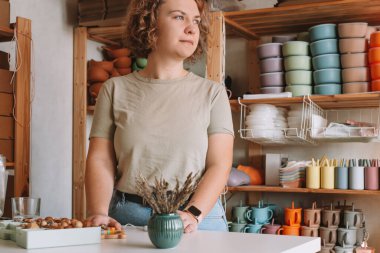 Ciddi yoğunlukta kıvırcık iş kadını kameraya bakıyor, satıcı işi, çocuklar için silikon sofra takımı. Atölye, küçük işletme. Renkli kaselerin, tabakların, bardakların, kaşıkların el yapımı tasarımı