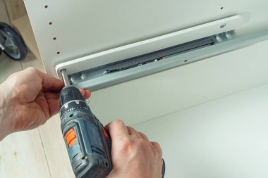 Erkek eller kablosuz elektrikli tornavida tutar, demiryolunu tamir etmek için vida takar, beyaz şifonyer ya da gardırop çekmecesi monte eder. Mobilyaların kendi kendine montajı, DIY, mobilya onarımı ve yeniden düzenleme