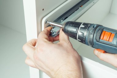 Erkek eller kablosuz elektrikli tornavida tutar, demiryolunu tamir etmek için vida takar, beyaz şifonyer ya da gardırop çekmecesi monte eder. Mobilyaların kendi kendine montajı, DIY, mobilya onarımı ve yeniden düzenleme