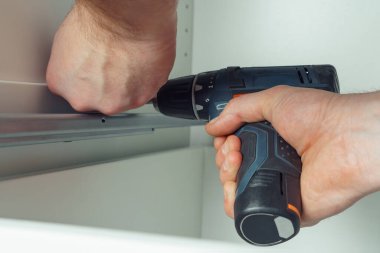 Erkek eller kablosuz elektrikli tornavida tutar, demiryolunu tamir etmek için vida takar, beyaz şifonyer ya da gardırop çekmecesi monte eder. Mobilyaların kendi kendine montajı, DIY, mobilya onarımı ve yeniden düzenleme