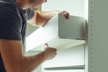 Erkek çekmecesi, parmaklıklara yerleştirip güvence altına alıyor, beyaz şifonyer ya da gardırop monte ediyor. Mobilyaların kendi kendine montajı, DIY, mobilya onarımı ve yeniden düzenleme
