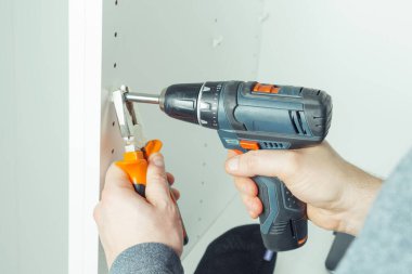 Erkek eller, beyaz raf, şifonyer ya da gardırop monte etmek için bir dizi deliğe plastik destek yerleştirmek üzere vidalarlar. Pense ile tornavida tutuyor. Mobilya montajı, DIY, yenileme