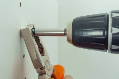 Beyaz raf, şifonyer ya da gardırop monte etmek için bir dizi deliğe plastik destek yerleştirmek üzere vidanın yakınlaştırılması. Penseyle tornavida tutuyorum. Mobilya montajı, DIY, yenileme