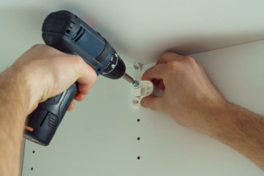Erkek eller, beyaz askı çubuğunu, şifonyeri ya da gardırobu tamir etmek için plastik destek yerleştirmek üzere vidalarlar. Tornavida tutuyor. Mobilya montajı, DIY, yenileme