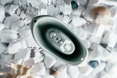 Altında beyaz taşlar ve deniz kabuğu olan suyun yüzeyinde delikleri olan şirin gri, küçük silikon bir tekne. Dalgaları ve benekleri olan şeffaf tatlı su. Üst Manzara. Oyuncak bebek, su oyunu