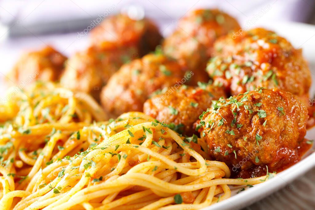Spaghetti pasta with meatballs in tomato sauce and herbs on a white plate.