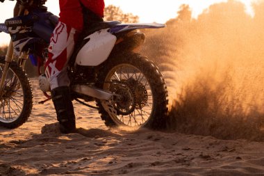 Bir motosikletçi gün batımında kum öğütür.