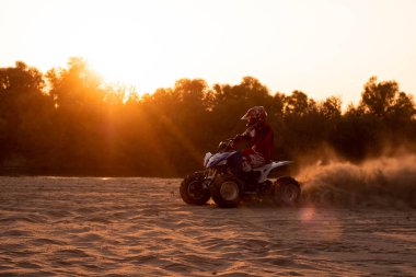 Bir motosikletçi gün batımında kum öğütür.
