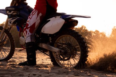 Bir motosikletçi gün batımında kum öğütür.